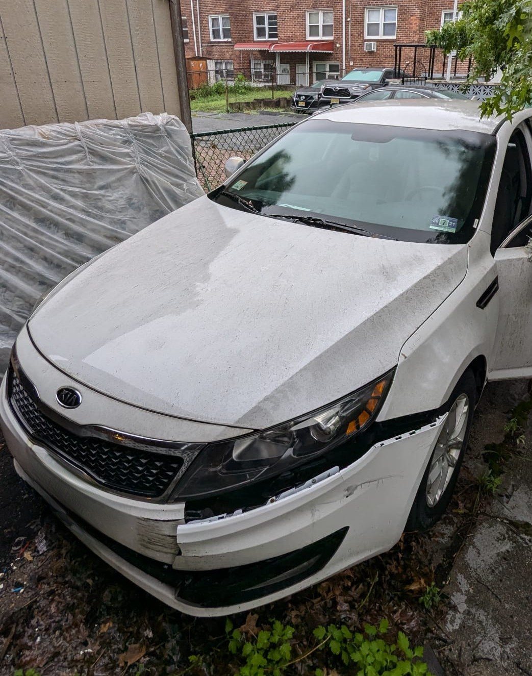 White Kia with front bumper and headlight damage, before repair