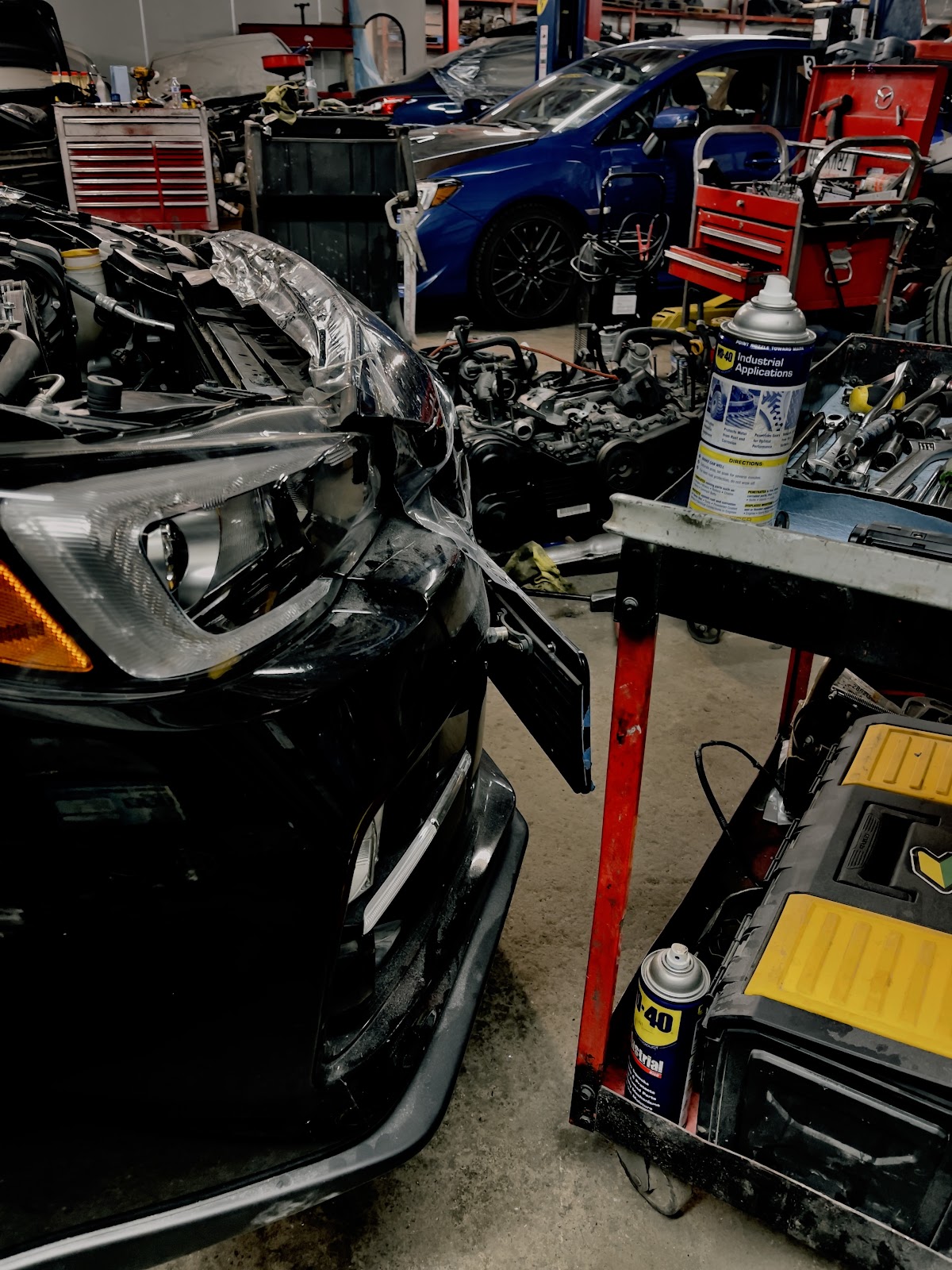 Front-end collision damage on a black sedan in the shop