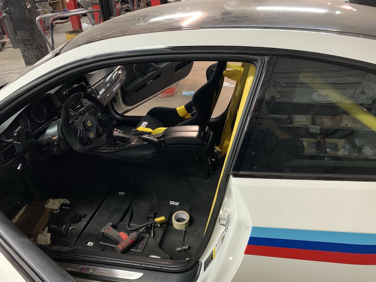 Roll cage and racing seat inside a white BMW M3 in the shop